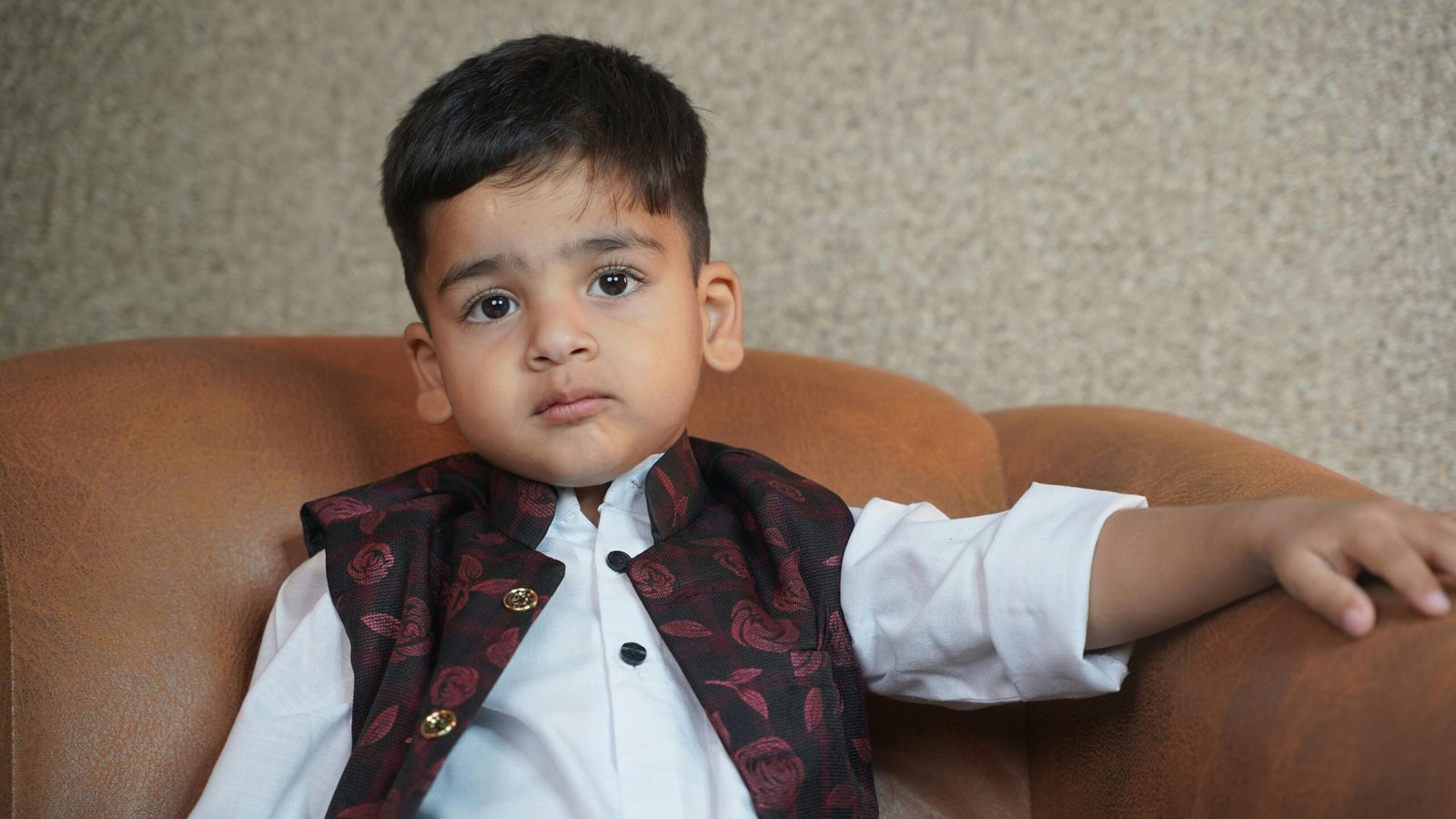 A young child in traditional clothing sitting on a couch, looking contemplative.